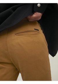 Bruna bomullbyxor med en mjuk textur, med en bakficka med horisontell öppning och en liten varumärkesetikett.