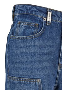 Denim-Jeans mit blauer Waschung, ausgestattet mit Kontrastnähten, einer Vordertasche und einem Etikett am Bund. Robustes Material, lässige Passform.