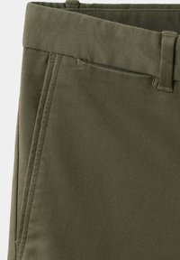 Gros plan de la taille d'un pantalon vert olive avec des passants de ceinture et un détail de poche avant en angle.