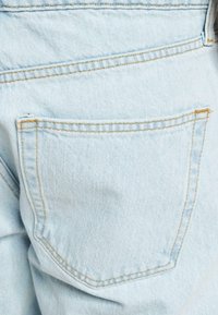 Jeansi din denim albastru deschis, cu un buzunar posterior cu cusături galbene contrastante, o textură netedă și un croi clasic.