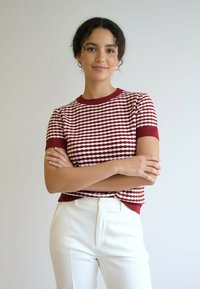 Sweter z krótkim rękawem w czerwono-białe paski, wykonany na drutach, z prążkowanym dekoltem i mankietami, zestawiony z białymi, dopasowanymi spodniami.