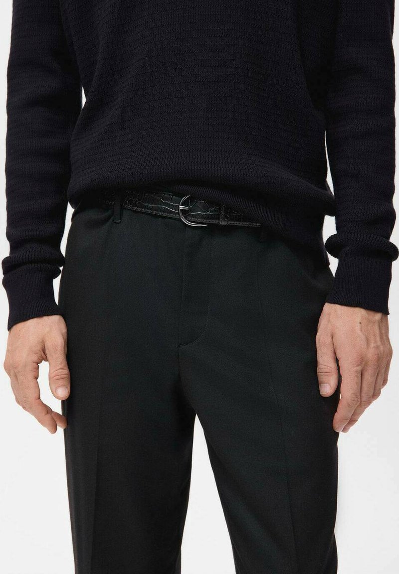 Maglione nero a trama con maniche lunghe abbinato a pantaloni scuri e una cintura nera con una fibbia rotonda in argento.