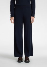 Laivastonsiniset leveälahkeiset housut, jotka on valmistettu pehmeästä materiaalista, ja joissa on sileä pinta sekä korkea vyötärö. Yhdistetty tummanruskeisiin paksupohjaisiin saappaisiin.