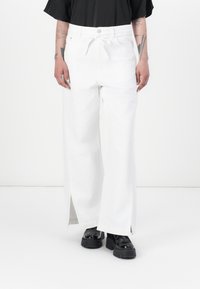 Hvite vide bukser laget av denim, med strikk i livet, sidelommer og glidelåser. Kombinert med svarte platåsko.