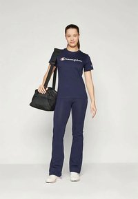 Μπλούζα Champion ναυτικού χρώματος με λευκό λογότυπο, συνδυασμένη με ναυτικές παντελόνες. Μαύρη τσάντα ώμου και ανοιχτόχρωμα παπούτσια. Απλός αθλητικός σχεδιασμός και εφαρμογή.