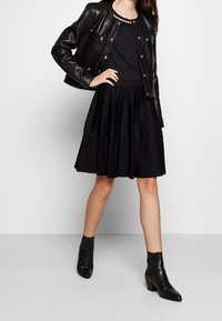 Svart läderjacka med metallknappar, kombinerad med en veckad svart kjol och texturerade svarta ankelstövlar. Enkel, monokrom outfit.