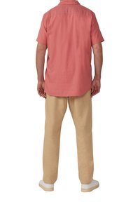 Korte mouw, koraalrode knopshirt gecombineerd met beige broeken, met een relaxte pasvorm en witte sneakers. Eenvoudig ontwerp, geen zichtbare patronen.
