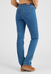 Vaqueros ajustados de denim azul con cintura de altura media, cinco bolsillos y un parche de ante en la parte posterior. Llevados con zapatillas de plataforma marrón.