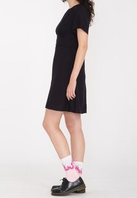 Abito nero a maniche corte con busto aderente e gonna a ruota. Abbinato a scarpe nere con lacci e calzini bianchi con fantasie di fiamme rosa.