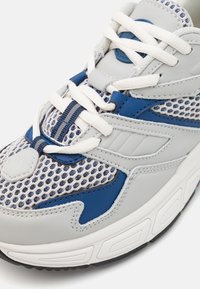 Leichte Sportnike mit grauen und blauenSynthetikmaterialien, Mesh-Einsätzen, weißen Schnürsenkeln und einer strukturierten Gummisohle mit Akzenten.