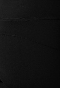 Czarne legginsy o gładkiej teksturze i dopasowanym kroju. Posiadają szew wzdłuż pleców, który dodaje kształtu i konturu.