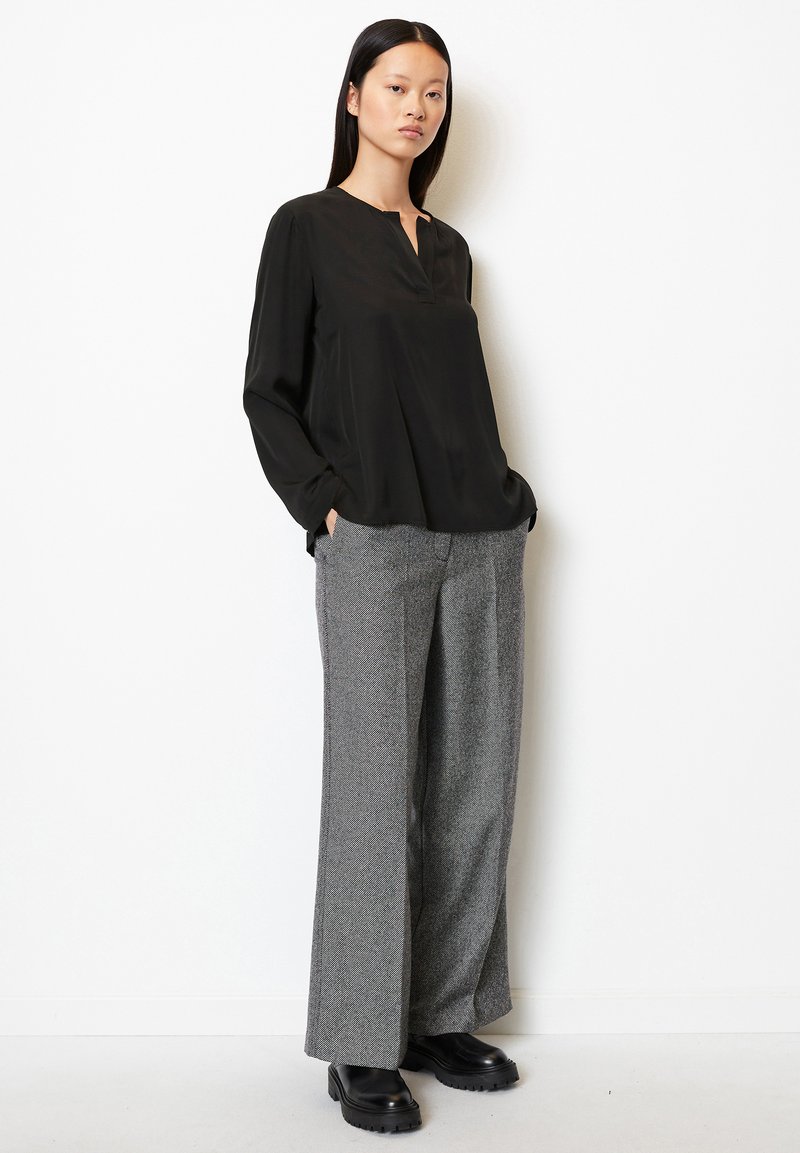 Czarny top z długim rękawem i kołnierzykiem w kształcie notcha, zestawiony z szarymi szerokimi spodniami teksturowanymi i masywnymi czarnymi botkami.