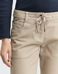 Beige Corduroy-Hosen mit einem Kordelzugbund, Fronttaschen und einem strukturierten Stoff. Sichtbare Nähte und Metallakzente an den Enden des Kordelzugs.