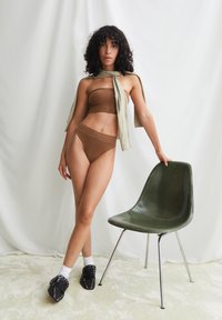 Bruine geribbelde bandeautop en bijpassende broekje met hoge taille, gecombineerd met zwarte slippers met studs en witte sokken, naast een groene stoel.