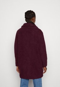Bordeaux faux pelsjakke med krave, lange ærmer og oversized snit, med en struktureret, blød yderside og længde under hoften.