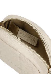 Beige leren pouch tas met een gestructureerde afwerking, gouden ritssluiting en een gevoerde binnenkant met een klein etiket dat erin is genaaid.