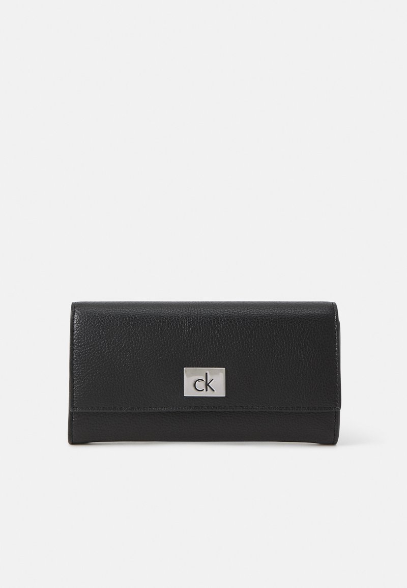Portefeuille en cuir noir avec une finition texturée, présentant une plaque logo "ck" en argent à l'avant, de forme rectangulaire et au design pliable.