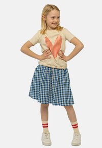 Camiseta beige con diseño de corazón a rayas rojas, combinada con una falda de cuadros azul y blanca, zapatillas blancas y calcetines a rayas rojas.