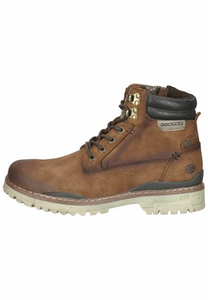 Bottine Dockers en cuir marron avec col noir matelassé, laçage devant avec œillets métalliques et semelle beige robuste avec motif de crampons.
