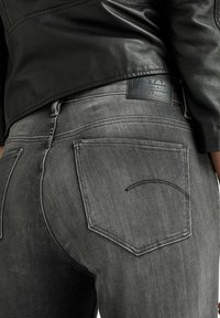 Gray denim jeans with a slight fade, featuring a leather patch with brand details, dual back pockets, and defined stitching.