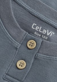 Graues Baumwollhemd mit Rundkragen, ausgestattet mit zwei Holzknöpfen und einem Etikett, das "CeLaVi Größe 100" zeigt. Glatte Textur.