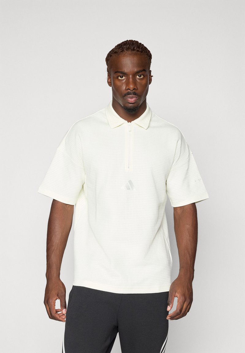 Polo majica s kratkim rukavima u svijetloj krem boji, teksturirani materijal s ovratnikom i polu-zatvaračem. Ima diskretni logotip na grudima.