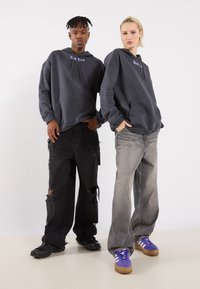 Grey hoodies with "New York" text, paired with distressed black and grey wide-leg jeans. Black and purple sneakers complete the outfits.