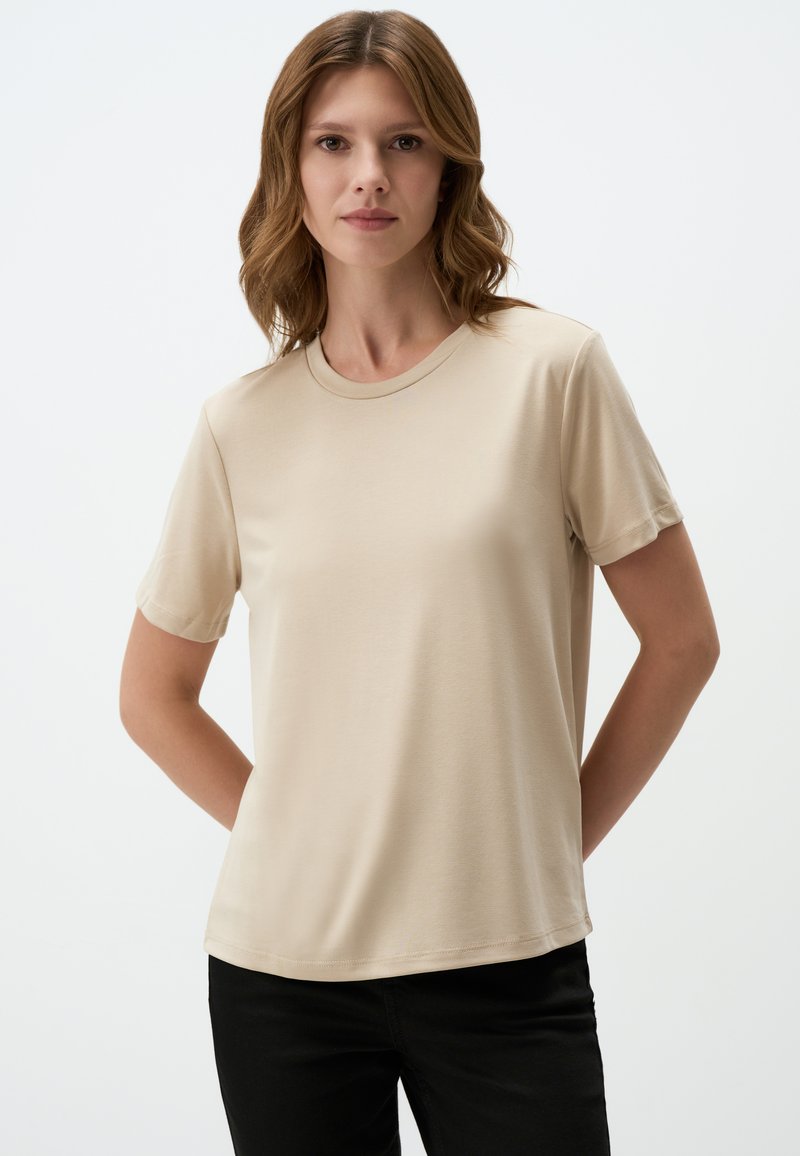 T-shirt beige a maniche corte con scollo rotondo, realizzata in tessuto morbido; abbinata a pantaloni neri. Design semplice e pulito senza motivi.