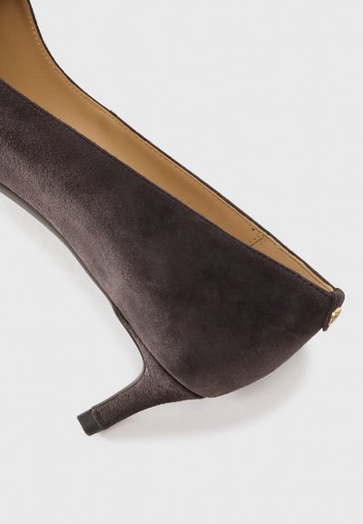 Chaussure à talon kitten en suède marron foncé avec un bout pointu et un bouton décoratif doré sur l'onglet du talon.