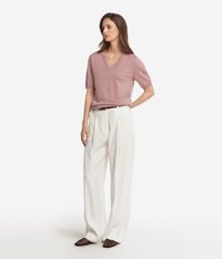 Ljusrosa kortärmad V-ringad tröja i kombination med vida vita byxor och bruna flätade slip-on skor, står framför en ljus bakgrund.