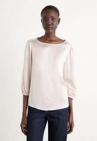 Light pink satin blouse with a boat neckline, three-quarter sleeves, and elastic cuffs, paired with dark blue denim trousers.