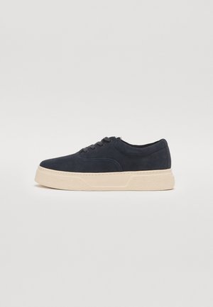 Marineblå semskede sneakers med en tykk beige gummisål, med avrundet tå og fem huller til snøring. Slett tekstur og minimalt design.