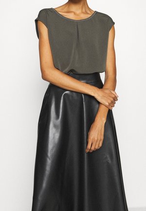 Blouse vert olive avec un col arrondi et des manches courtes, associée à une jupe en cuir noir brillant taille haute. Texture lisse, plis subtils.