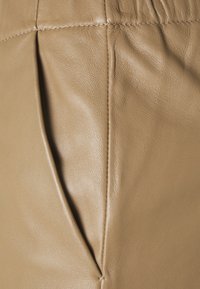 Beige leren materiaal met een zachte textuur, met plooien en zichtbare stiksels langs de naden. Gladde oppervlakte zonder patronen of bevestigingsmiddelen.