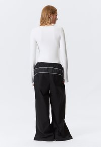 Langarm-weißes Oberteil kombiniert mit schwarzen, weit geschnittenen Hosen mit Tunnelzugbund und weißen Akzentstreifen auf der Rückseite.