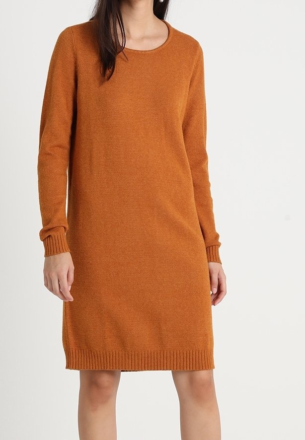Femme portant une robe en maille couleur rouille, à manches longues et longueur au genou, avec des poignets et un ourlet côtelés, debout devant un fond uni.
