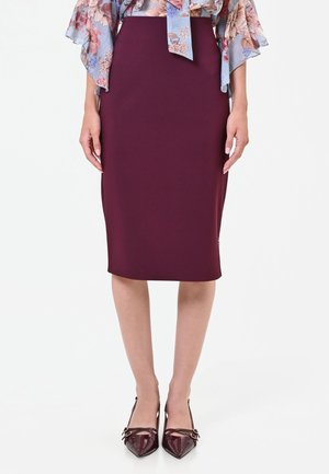 Donna che indossa una gonna a matita aderente bordeaux a lunghezza ginocchio, una camicetta floreale con maniche larghe e décolleté bordeaux con punta appuntita e fiocchi.