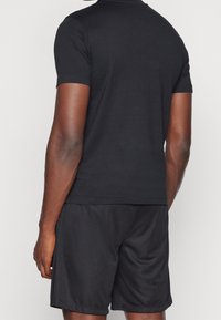 Černé tričko s krátkým rukávem a kulatým výstřihem v kombinaci s černými šortkami. Tkanina se zdá být hladká a lehká, vhodná pro neformální nošení.