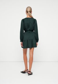 Dark green dress with long sleeves, a fitted bodice, and a tiered skirt. Made of smooth fabric with a waist tie. Features a square back design.