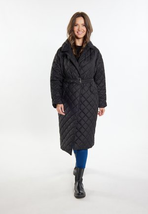 Schwarzer gesteppter langer Mantel mit tailliertem Gürtel, großem Kragen und Rautenmuster. Tragend über blauen Jeans und schwarzen Stiefeletten.