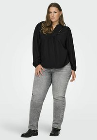 Blusa nera a maniche lunghe con design plissettato e scollatura a v, abbinata a jeans grigi a gamba dritta e stivaletti neri.