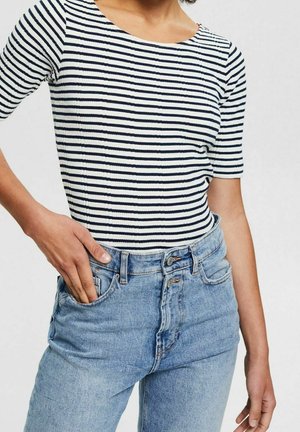 Gestreept kort mouw shirt in marineblauw en wit ribstof, gecombineerd met lichtblauwe, hooggetailleerde jeans met knopen en een vervaagde textuur.