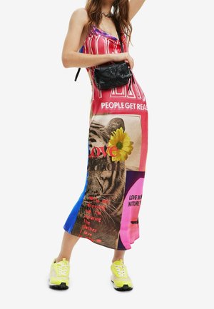Robe midi multicolore avec un mélange d'imprimés graphiques et de textes, agrémentée d'une accent floral. Portée avec un sac bandoulière noir et des baskets néon.