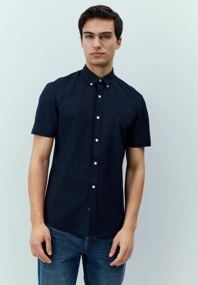 Kurzärmliges navy Button-Up-Hemd aus Baumwolle. Verfügt über einen klassischen Kragen und eine einzelne Brusttasche, kombiniert mit blauen Jeans.