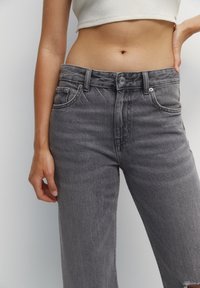 Jean en denim gris taille haute avec un léger effet usé, comportant cinq poches et une fermeture à boutons. Tissu doux et texturé.