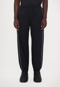 Zwarte sportbroek met een gestructureerde afwerking, voorzien van witte zijstrepen en een elastische tailleband. Aansluitend bij de enkels.