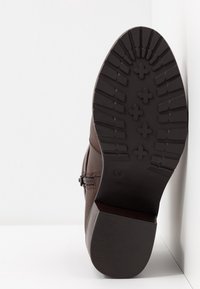 Bota de cuero marrón con suela de goma texturizada, patrón de banda de rodadura visible y cremallera lateral para ponérsela fácilmente. El diseño es simple y funcional.