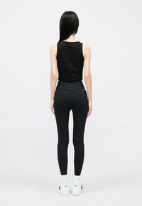 Fekete ujjatlan felső magas derekú fekete leggingsszel párosítva. Sima textúra, tiszta vonalak, fehér sportcipőkkel, logó díszítéssel.