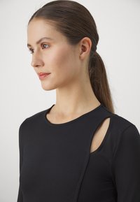 Black long-sleeve top with a smooth texture, features an asymmetrical cut-out design at the shoulder, finished with a rounded neckline.