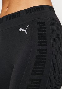 Černé legíny s texturovaným povrchem, které mají výrazné logo na pase a síťovaný vzor na straně pro zvýšení prodyšnosti.